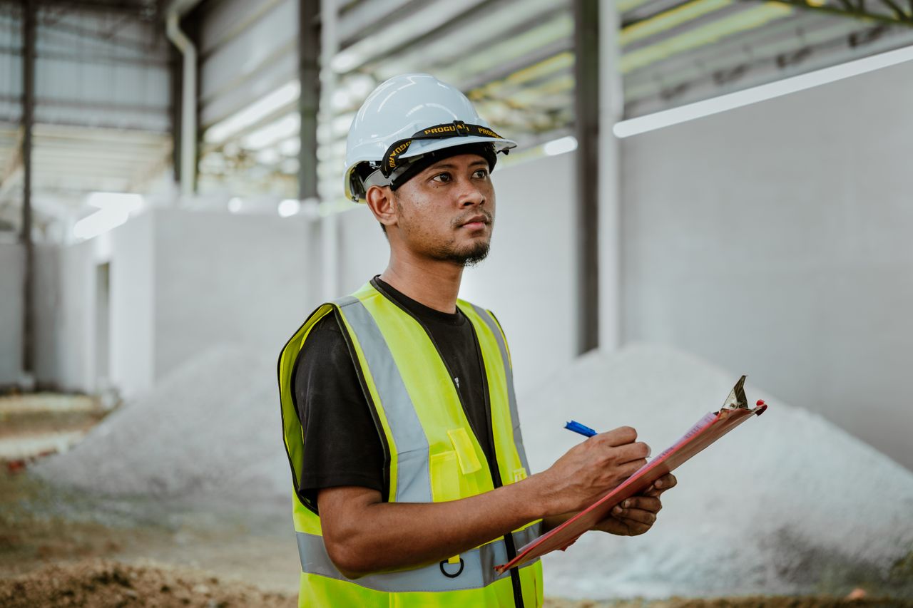 Asian construction worker in a factory setting, using a clipboard for inspection tasks in Banting, Malaysia.