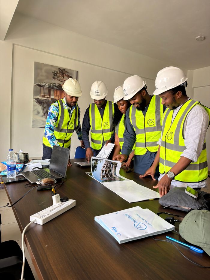 A group of engineers in safety gear examines architectural plans in an office.