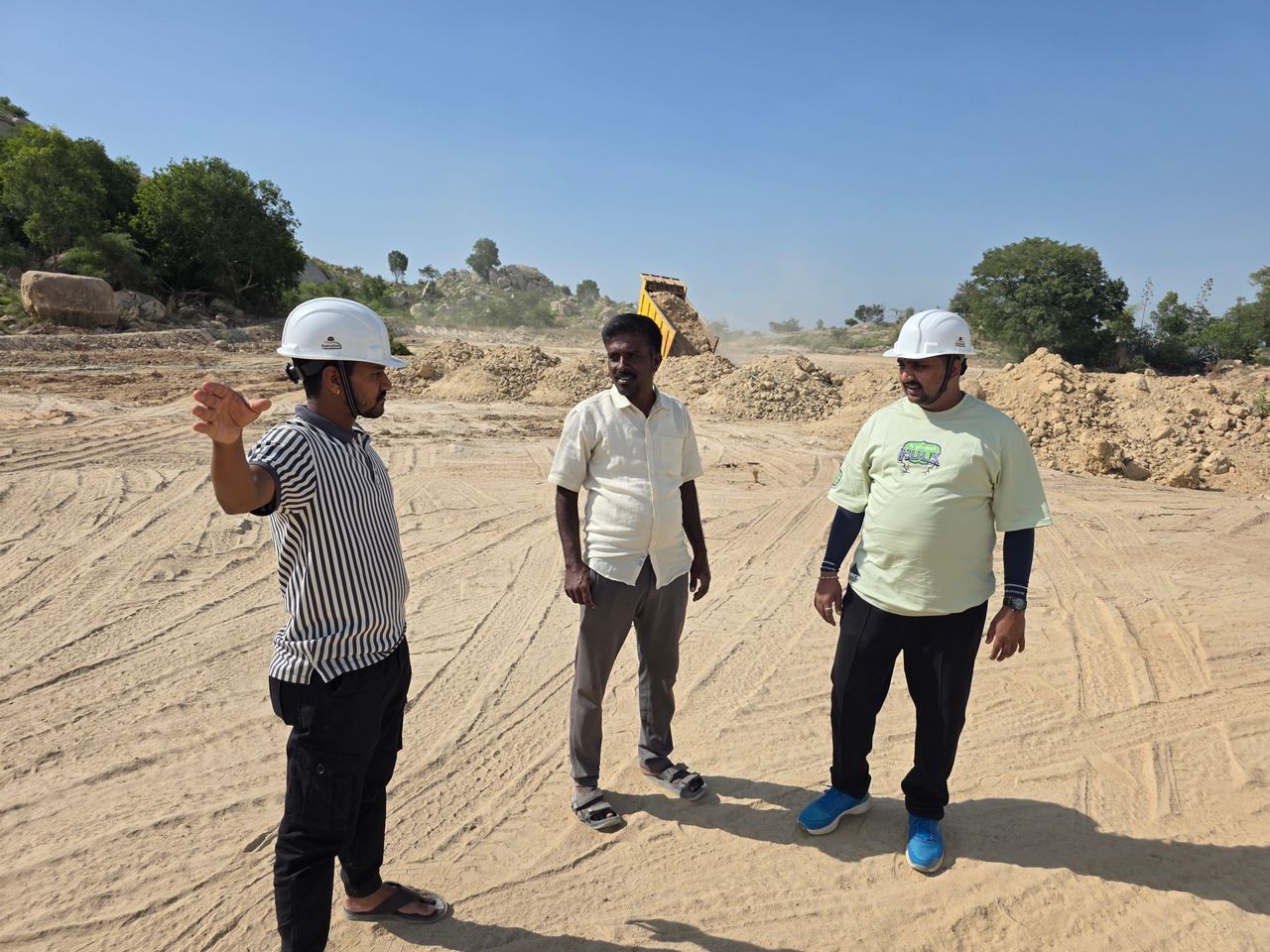 Engineers discussing a construction project at a sandy outdoor site, wearing hard hats for safety.